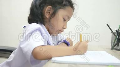 亚洲小女孩穿着泰国学生制服在木桌上做作业，选择焦点浅田深
